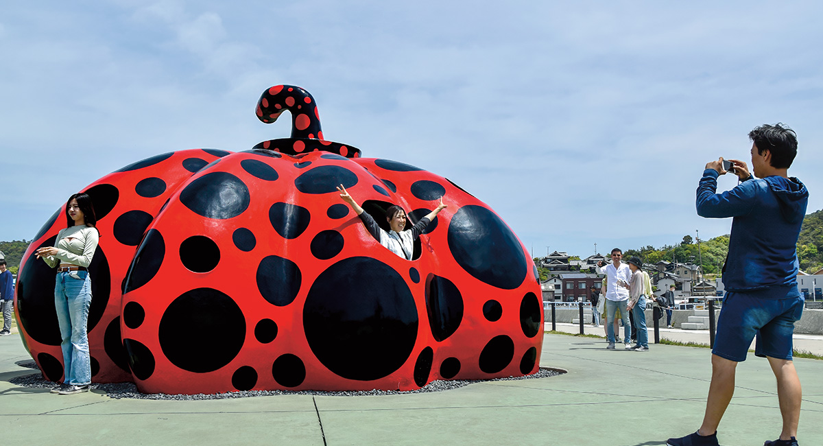 Image of a huge black and red polka-dotted pumpkin with people taking photos in front of