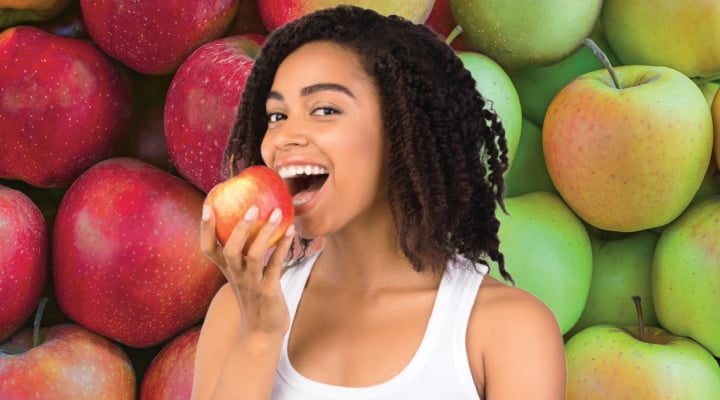 A woman holds a red apple up to her open mouth, surrounded by red and green apples
