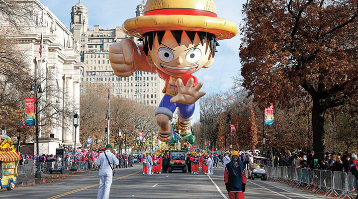 A large Monkey D. Luffy balloon floats above a city parade route lined with crowds