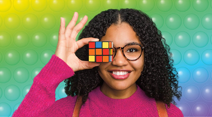 A young woman holds a Rubik's cube in front of one eye